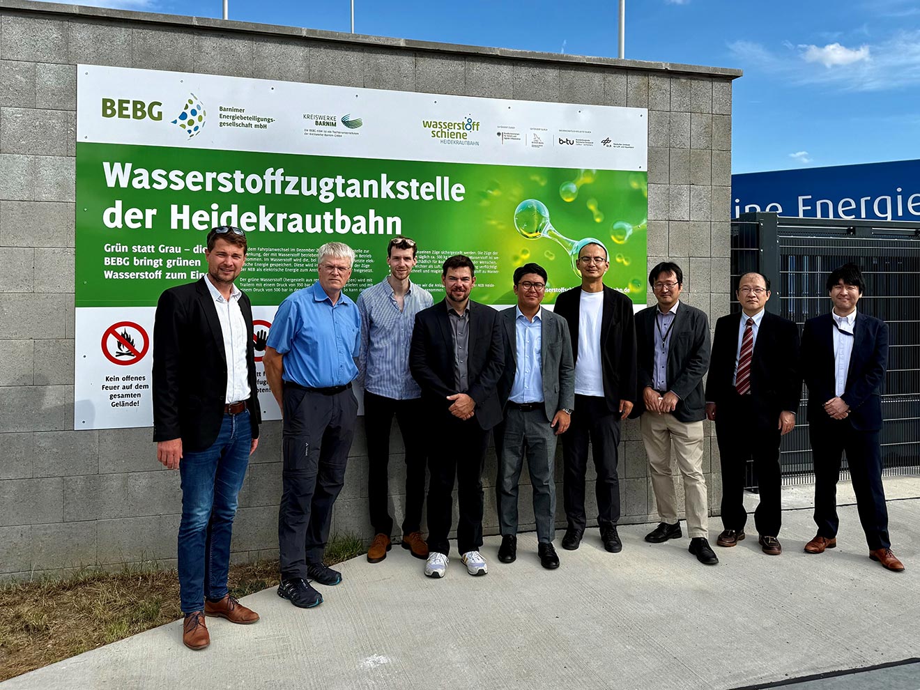 Gruppenfoto einer japanischen Delegation mit deutschen Partnern vor der Wasserstofftankstelle der Heidekrautbahn in Basdorf.